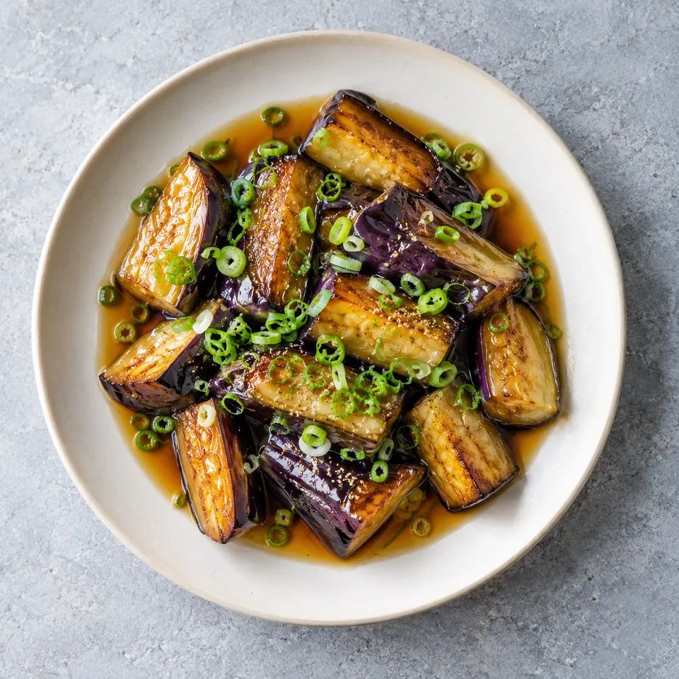 Agebitashi d’aubergines dorées : tronçons fondants nappés de sauce, parsemés de ciboule sur assiette blanche.