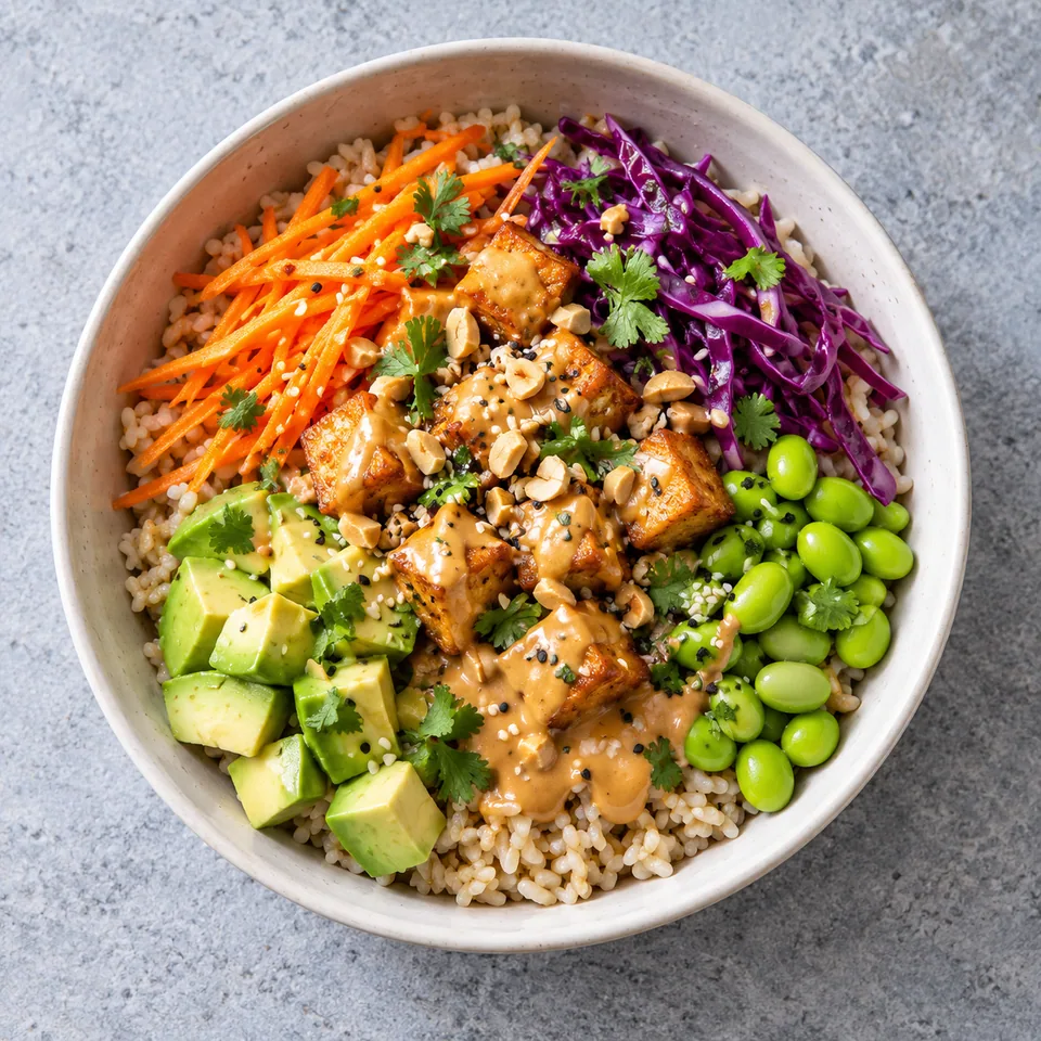 Bol de riz complet, tofu doré, edamame, chou rouge et avocat nappé de sauce cacahuète.