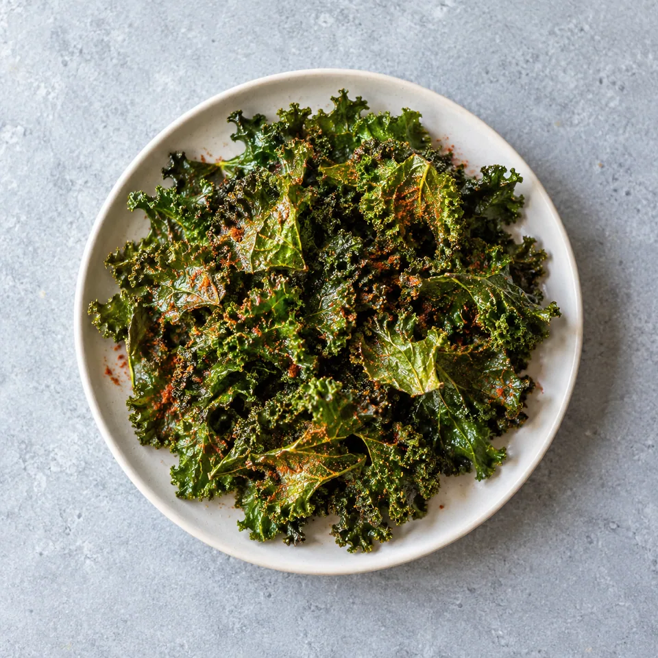 Chips de chou kale croustillantes vert foncé parsemées de paprika rouge sur une assiette blanche.