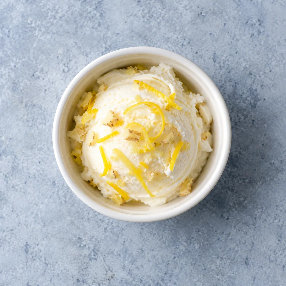 Portion de glacé au citron et gingembre dans un ramequin, parsemée de zestes jaunes et d'éclats de gingembre.
