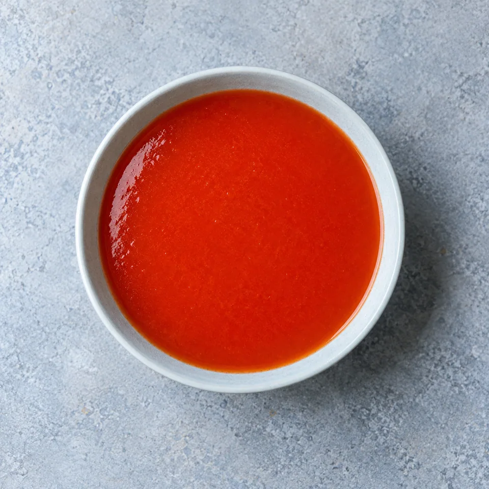 Bol de gaspacho de tomates rouge lisse et brillant, servi froid dans un récipient blanc.