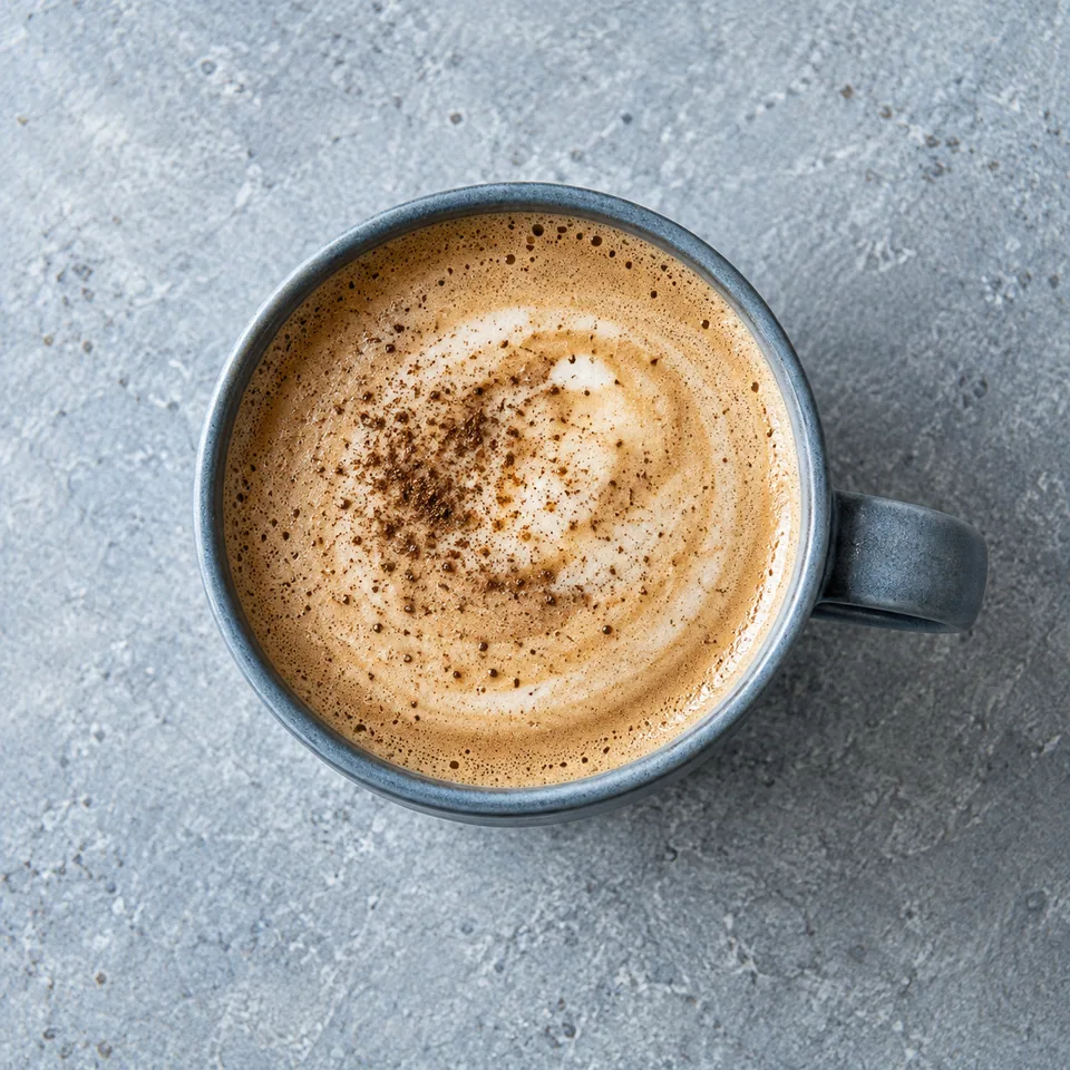 Hojicha latte chaud à l’avoine dans un mug bleu-gris, surface mousseuse et dorée.