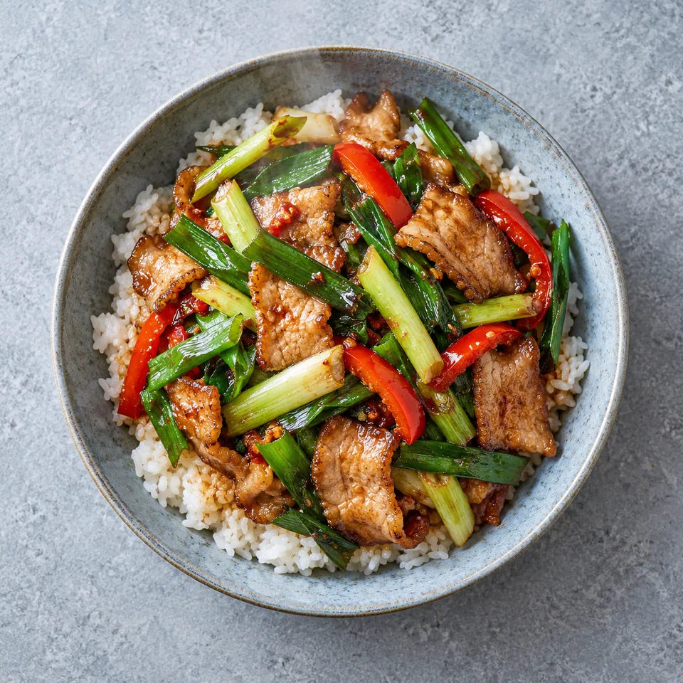 Hui guo rou : riz blanc recouvert de porc sauté aux poireaux et poivrons rouges sur assiette bleue.