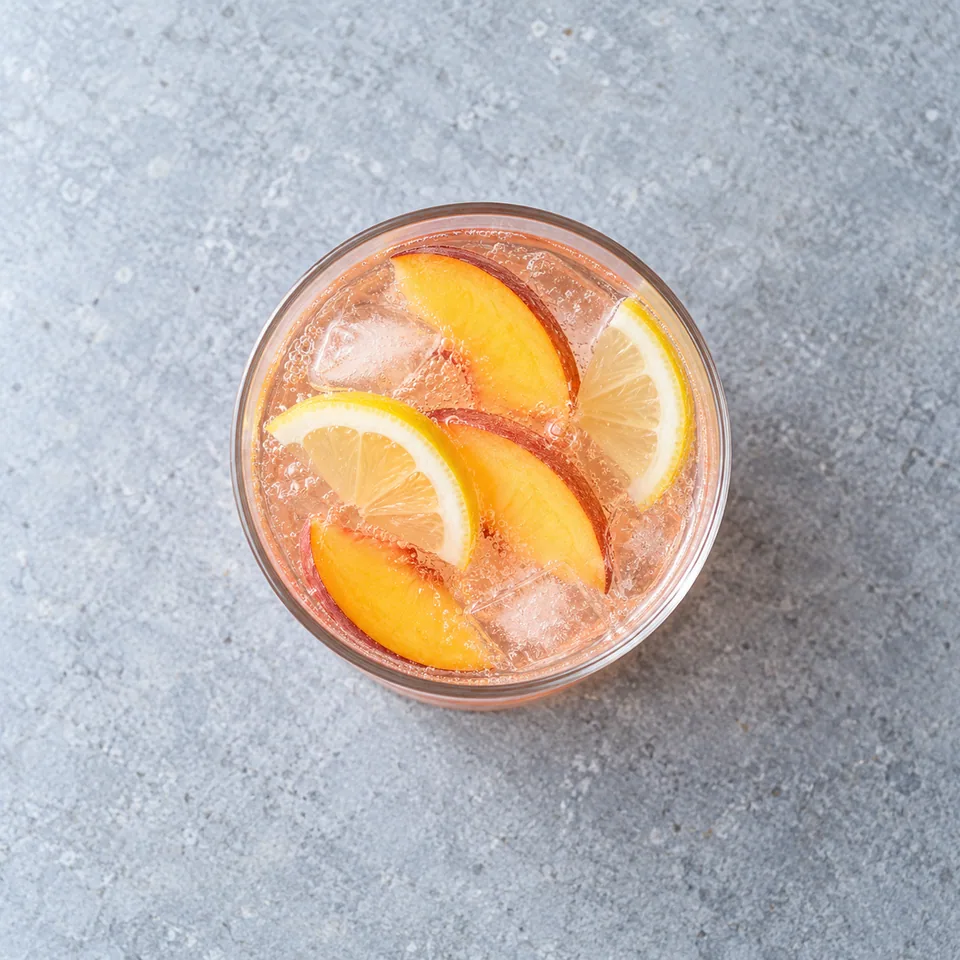 Limonade à la pêche : verre de boisson rosée pétillante garni de tranches de pêche et de citron.