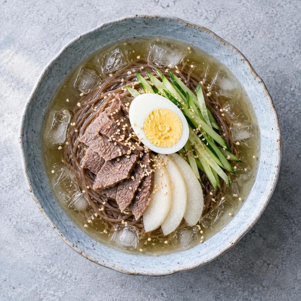 Naengmyeon : nouilles froides coréennes au bœuf, concombre, poire et œuf dur dans un bol en grès bleu-gris.