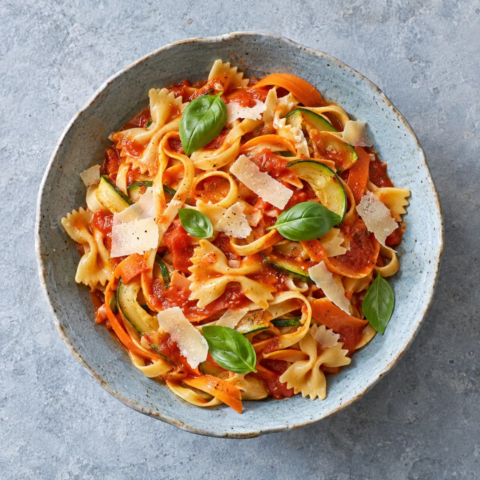 Bol de pâtes fraîches maison tagliatelles et farfalle à la sauce tomate cachée aux légumes, garnie de fromage et basilic.