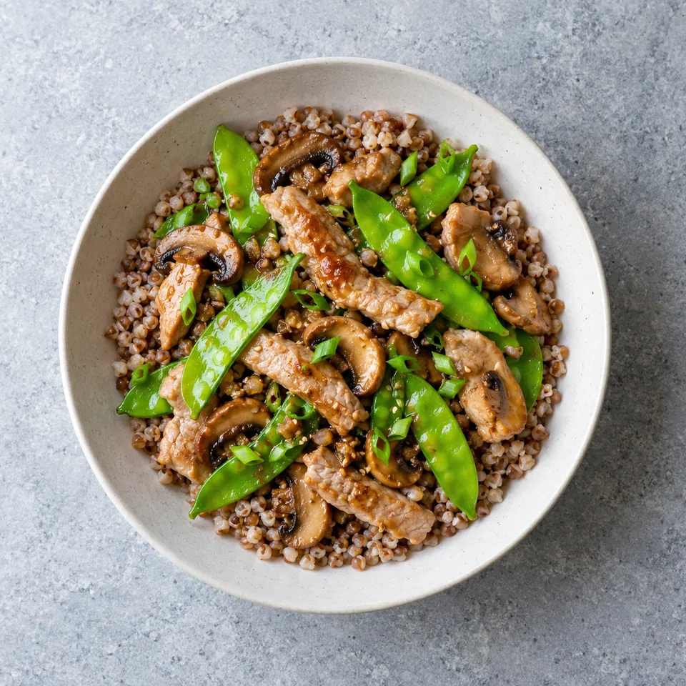 Porc sauté en lamelles avec pois gourmands et champignons, servi sur un lit de sarrasin cuit.