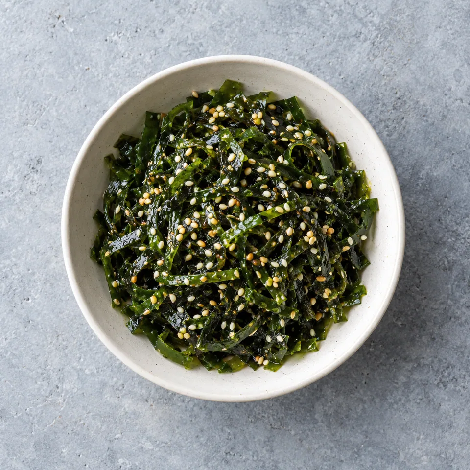 Salade d’algues au sésame : lamelles d'algues vert foncé brillantes parsemées de graines de sésame dans un bol blanc.