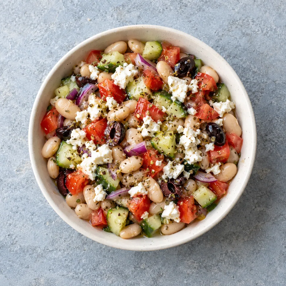 Salade de haricots blancs à la feta, en bol, avec dés de tomate et concombre, oignon rouge, olives noires et feta émiettée.