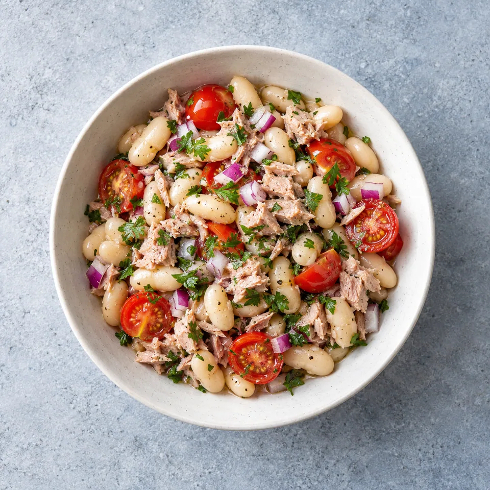 Salade de haricots blancs au thon dans un bol, avec tomates cerises, oignon rouge et persil.
