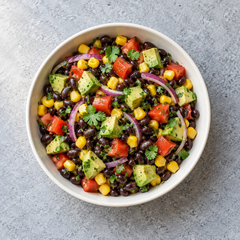 Salade de haricots noirs, avocat et maïs en bol, avec dés de tomates rouges, oignon rouge émincé et coriandre ciselée.