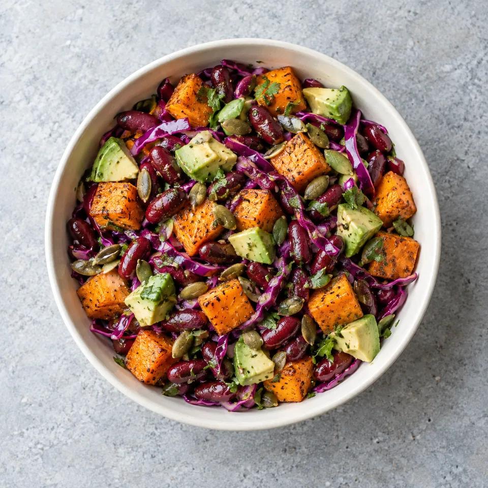 Salade de haricots rouges et patate douce en bol, avec chou rouge émincé, dés d’avocat et graines de courge.