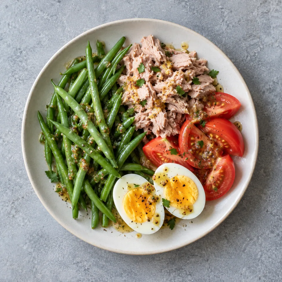 Salade de thon, haricots verts et œufs : haricots, quartiers de tomates, thon et deux moitiés d’œuf nappés de vinaigrette.