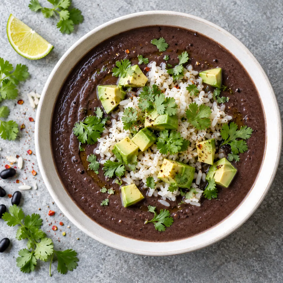 Bol de sopa negra crème de haricots noirs avec riz, dés d'avocat et coriandre sur fond blanc cassé.