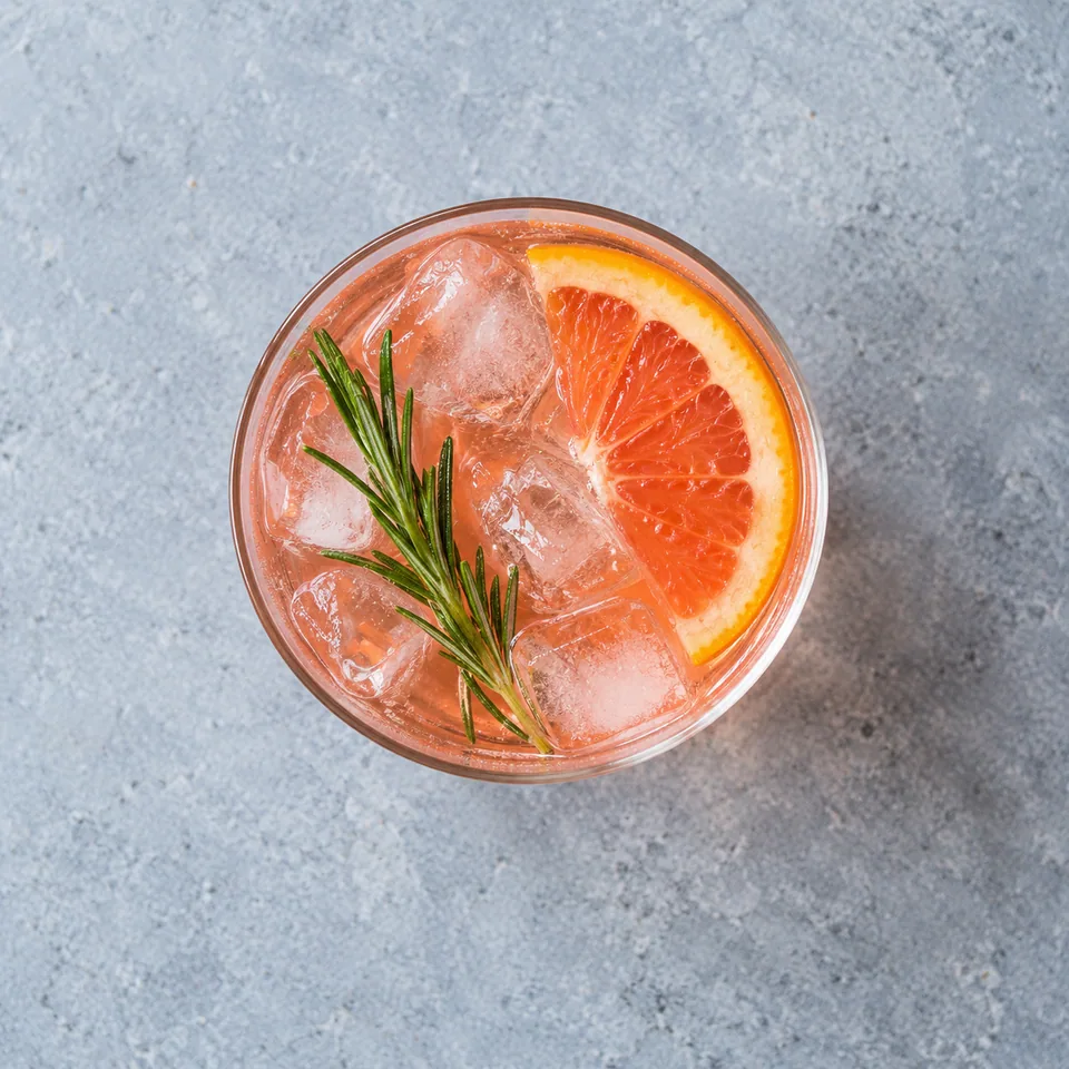 Spritz sans alcool pamplemousse-romarin : verre avec liquide rose, glaçons et rondelle d'orange.