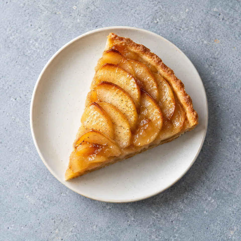 Part de tarte aux pommes à la compote avec rondelles de pommes caramélisées et graines de vanille visibles sur une assiette.
