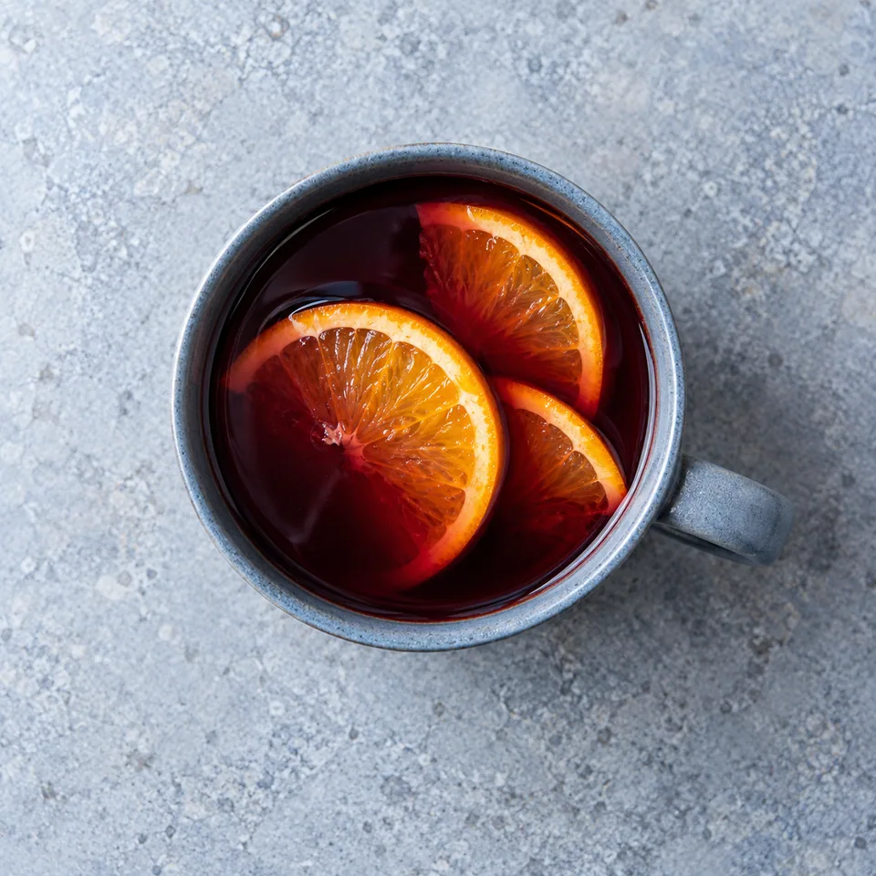 Vin chaud aux épices, orange et clou de girofle dans un mug bleu-gris avec des rondelles d'orange.