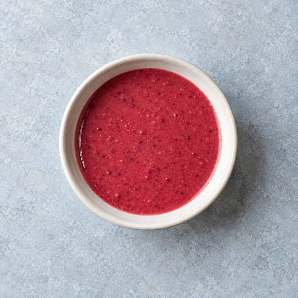 Vinaigrette framboise et balsamique, sauce rose violacée homogène dans un petit bol.