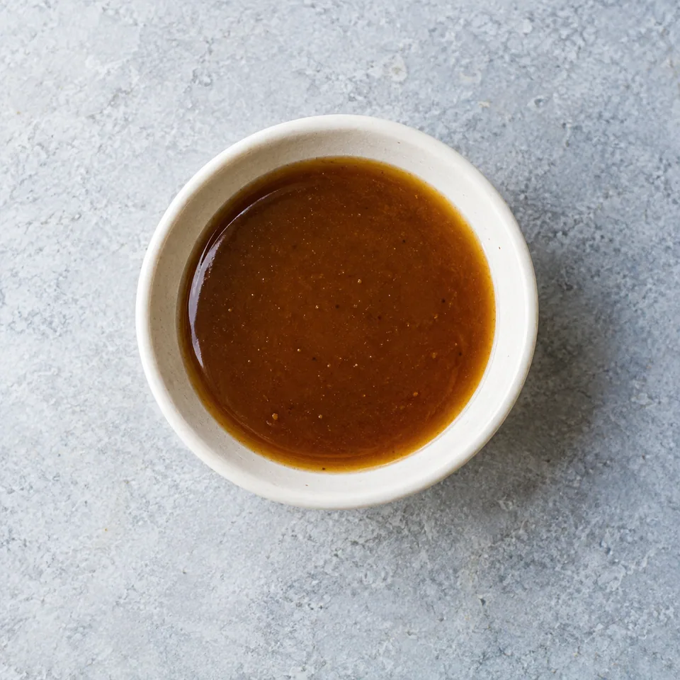Vinaigrette miel-balsamique : petite portion de sauce lisse, brillante et brun ambré dans un bol.