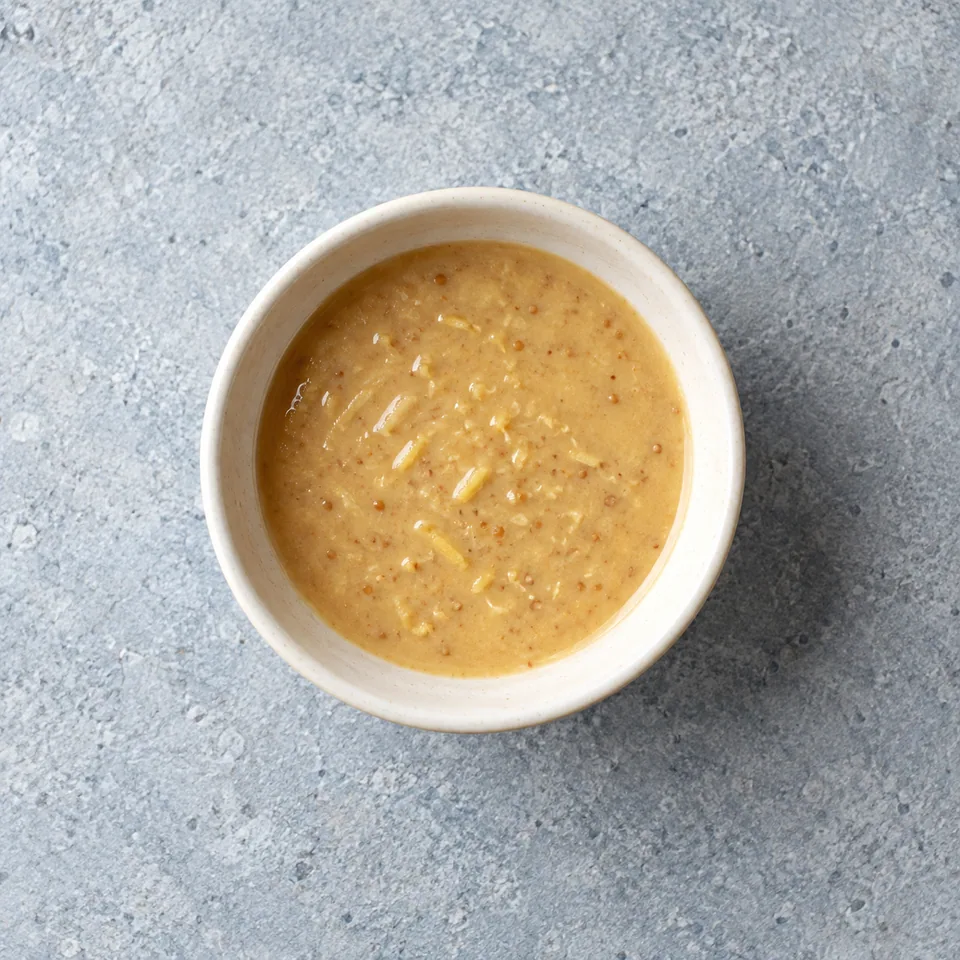 Vinaigrette miso-citron beige clair et brillante, avec de fines particules de gingembre, servie dans un petit bol.