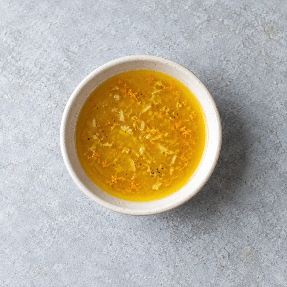 Vinaigrette orange-gingembre jaune orangé, homogène et brillante, avec de fines particules de gingembre dans un petit bol.