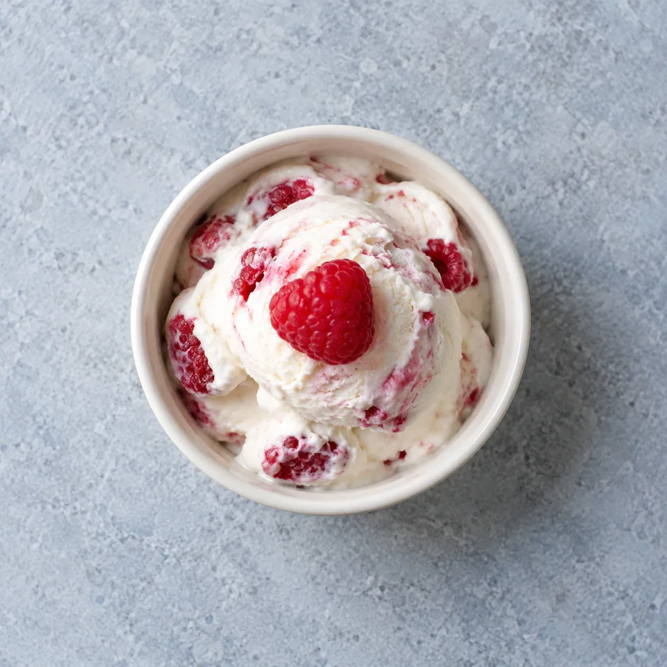 Yaourt glacé aux framboises : ramequin blanc avec framboises rouges entières, décoré d'une framboise fraîche sur le dessus.